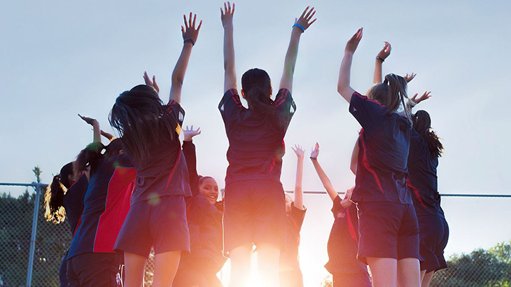 Young netball players raising their hands in a huddle. 