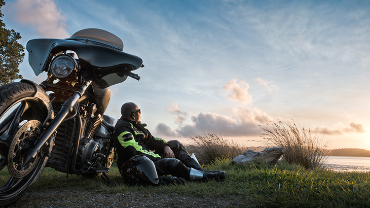 Motorcycle 1 Motorcyclists sits on grass, leaning against his bike.