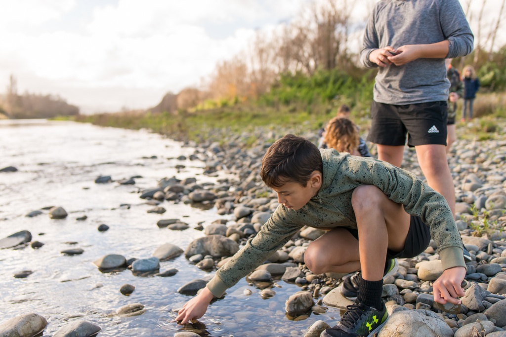 Boy crouching at a river to collect a stone