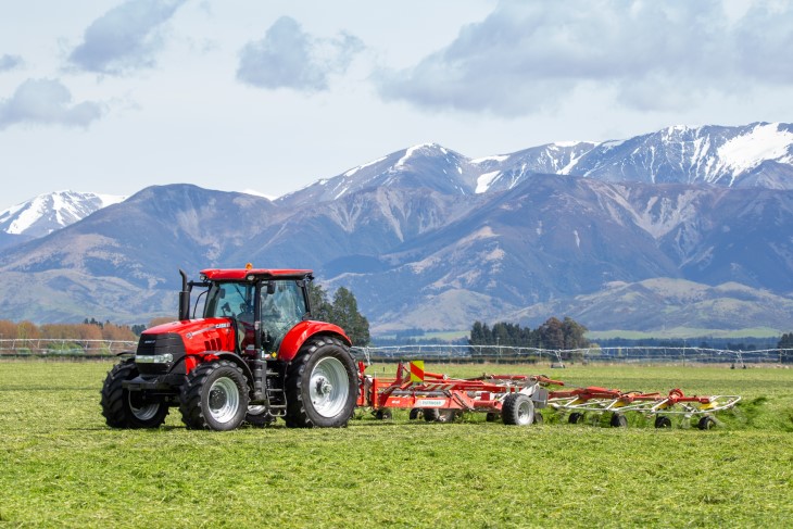 A tractor ploughing a field on a farm in front of mountain ranges.